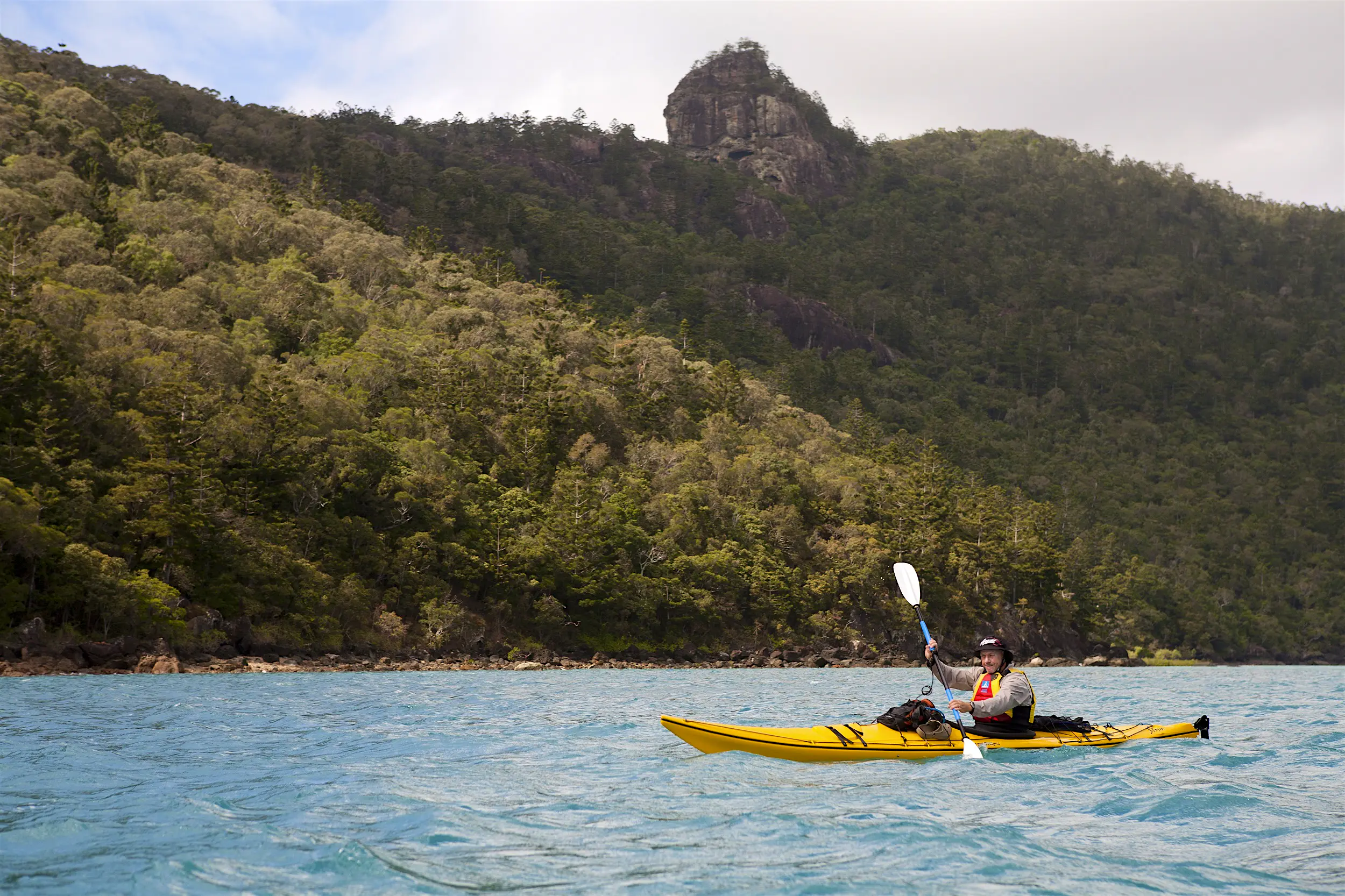 Whitsundays paddling.jpg A man paddles a yellow sea kayak across choppy waters with a forested island of the Whitsundays in the background.
