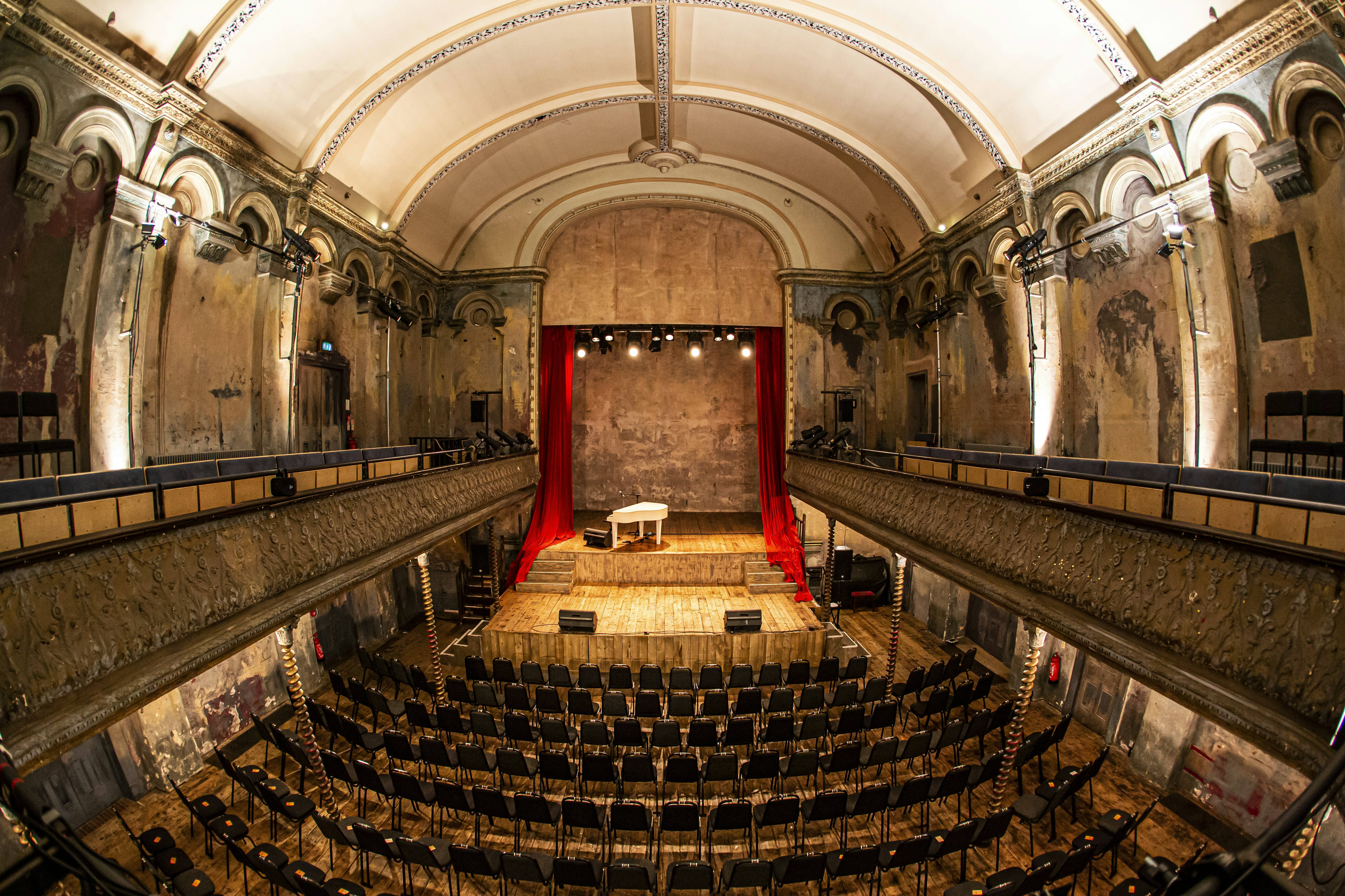 Inuti Wiltons Music Hall;  bilden är tagen med fisheye-lins från en balkong och tittar ner på stolar som är uppställda för en konsert.