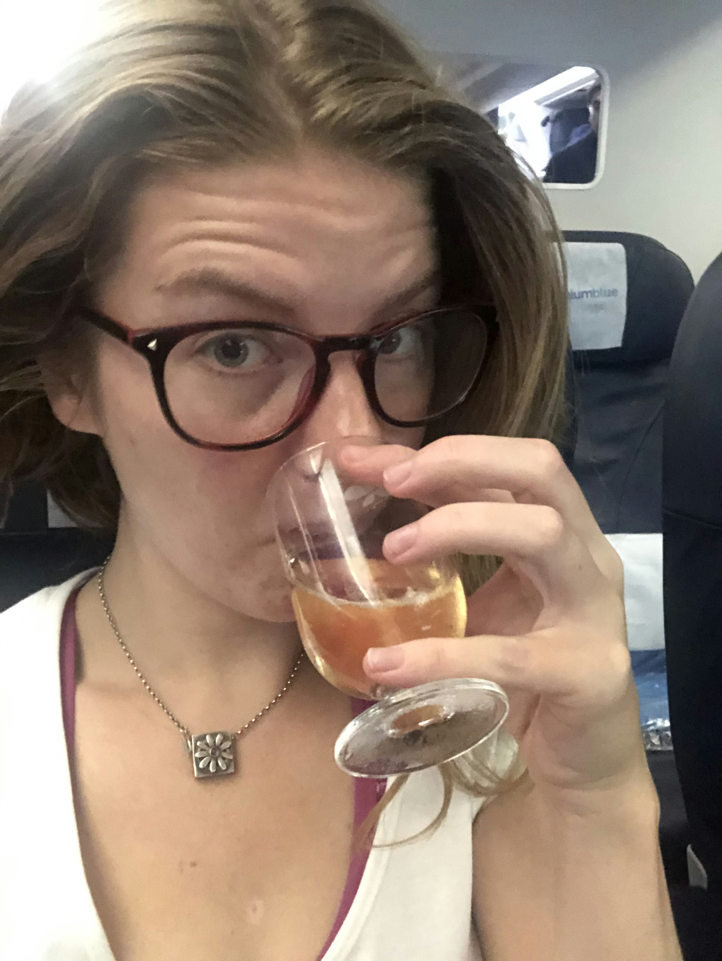 A woman sips a glass of wine on a plane