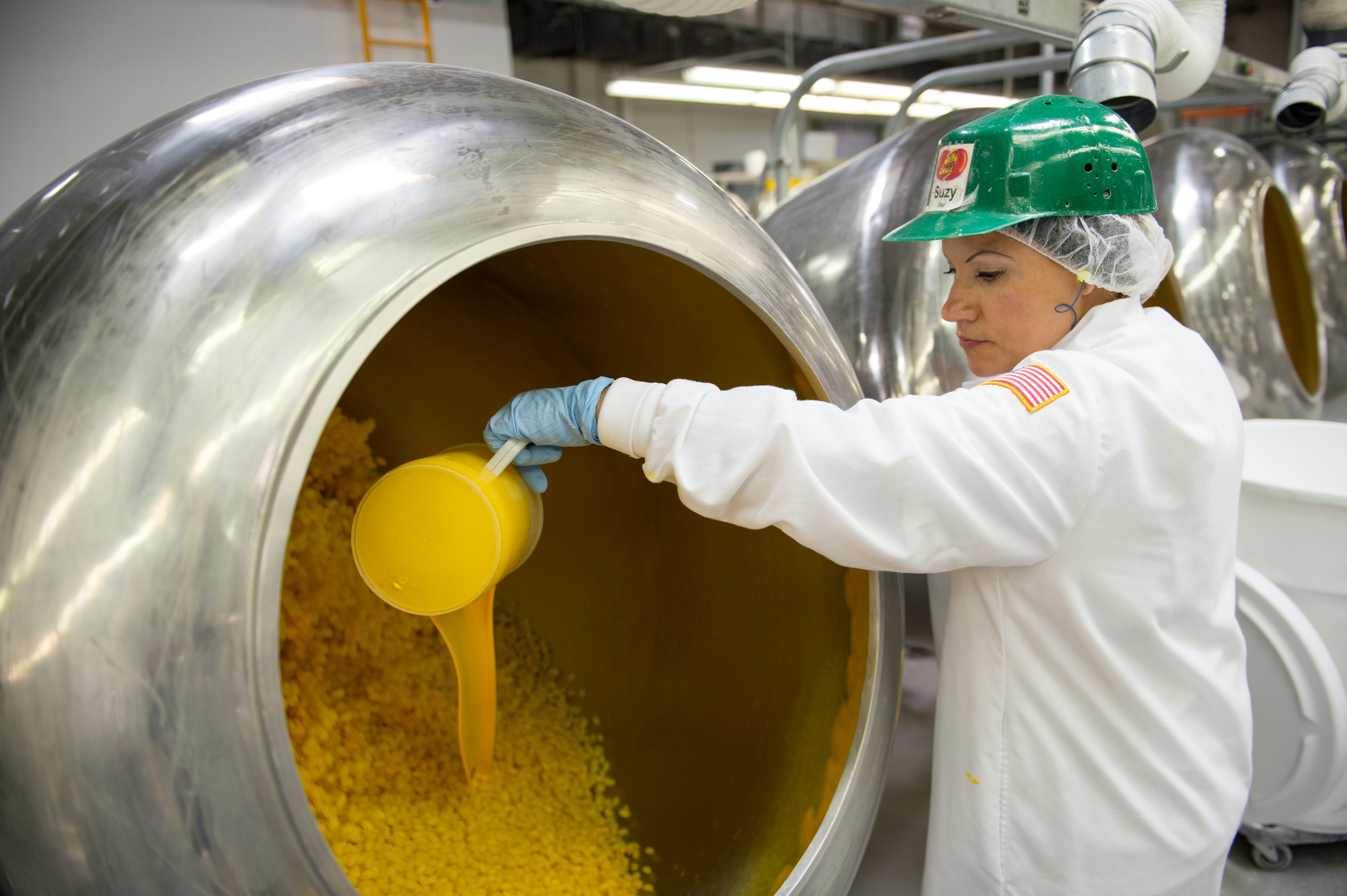 A woman in a sterile suit pours yellow liquid into a batch of jelly beans