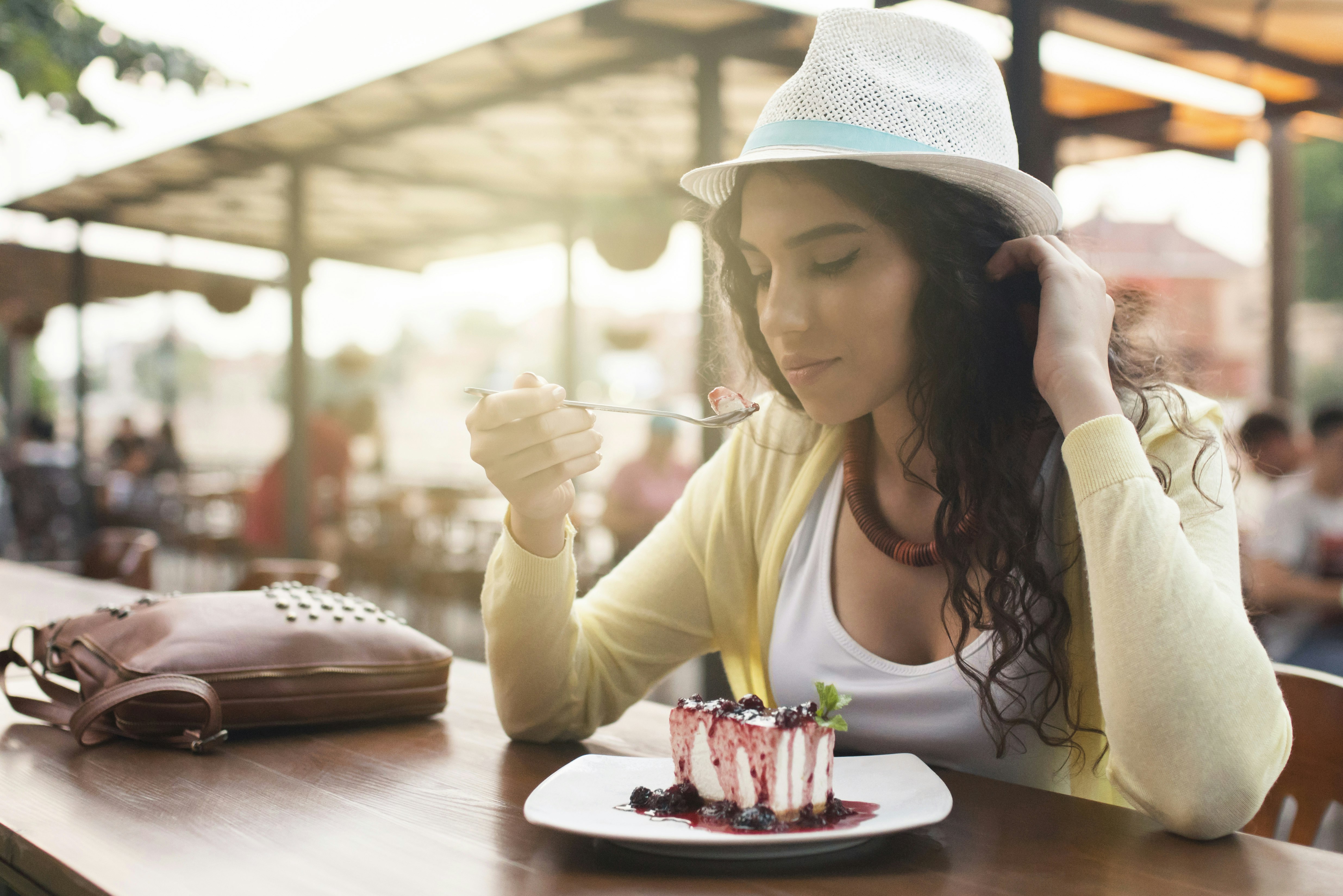 En kvinnlig resenär sitter ensam vid ett stort träbord och äter cheesecake med en gaffel