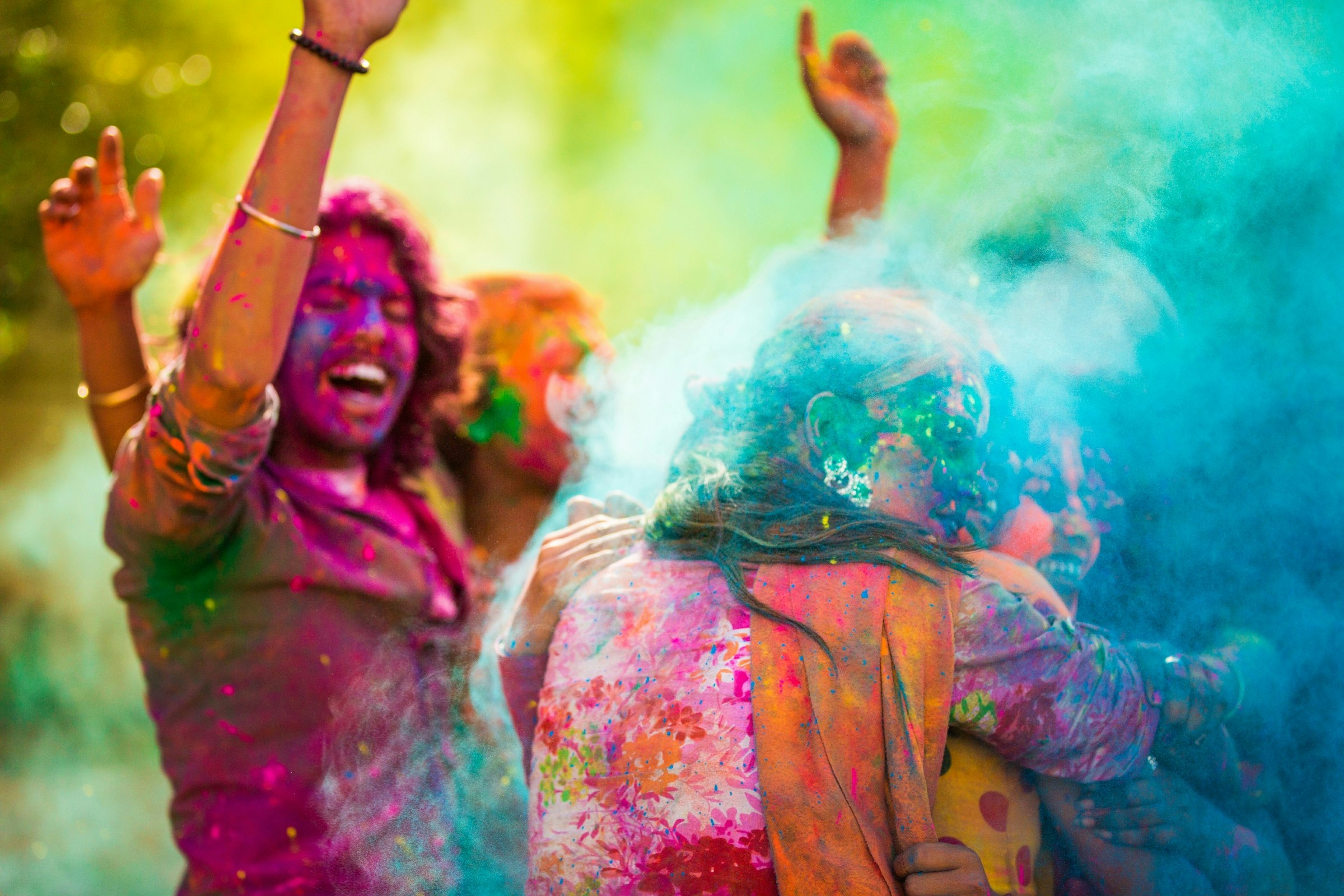 Three girls, embracing one another, are cloaked in coloured powder which has been poured over them by a friend during Holi celebrations.