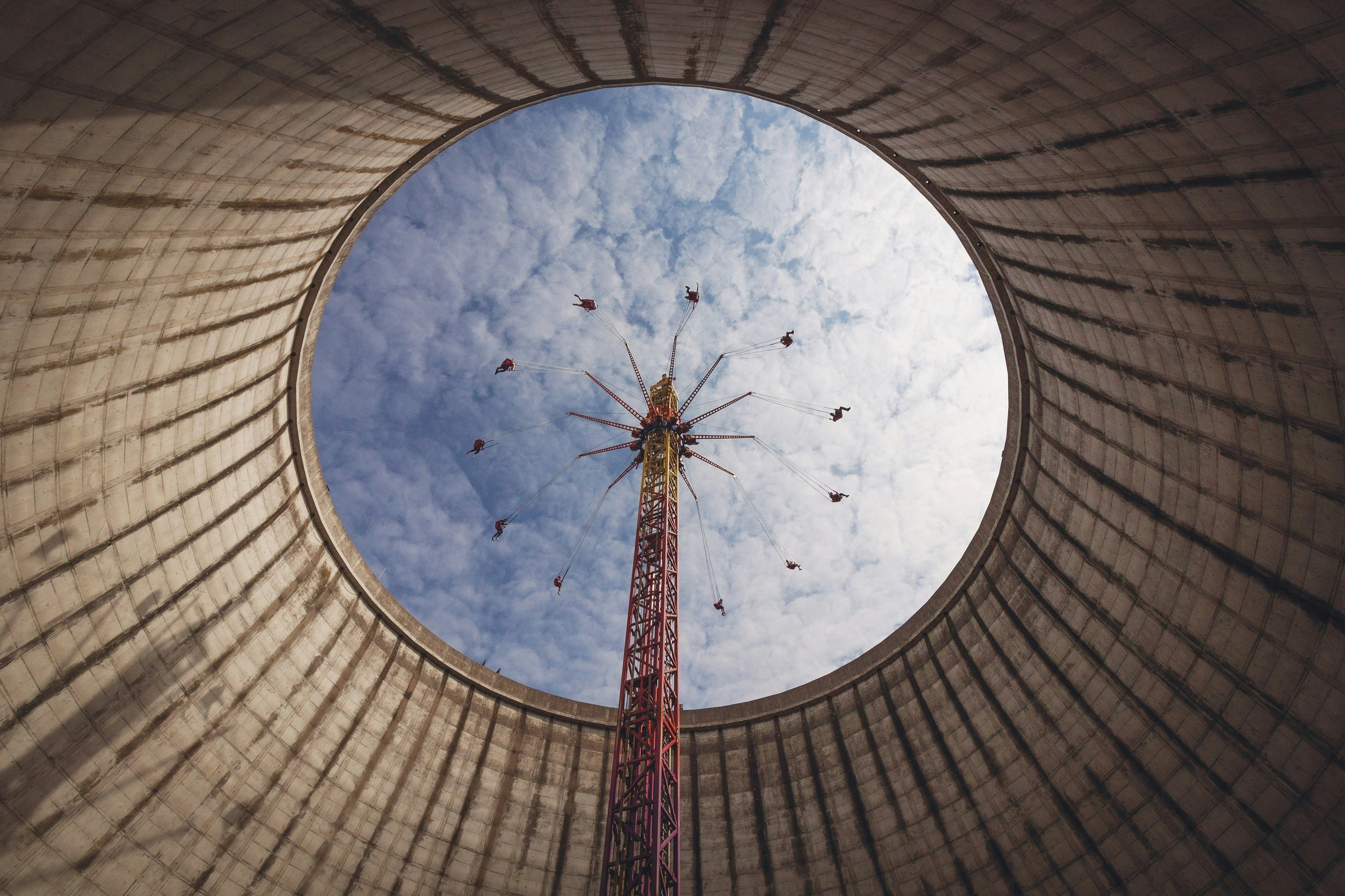 An upwards shot taken within the huge cooling tower of an ex-power plant, with people on swings of a fairground ride at the top.