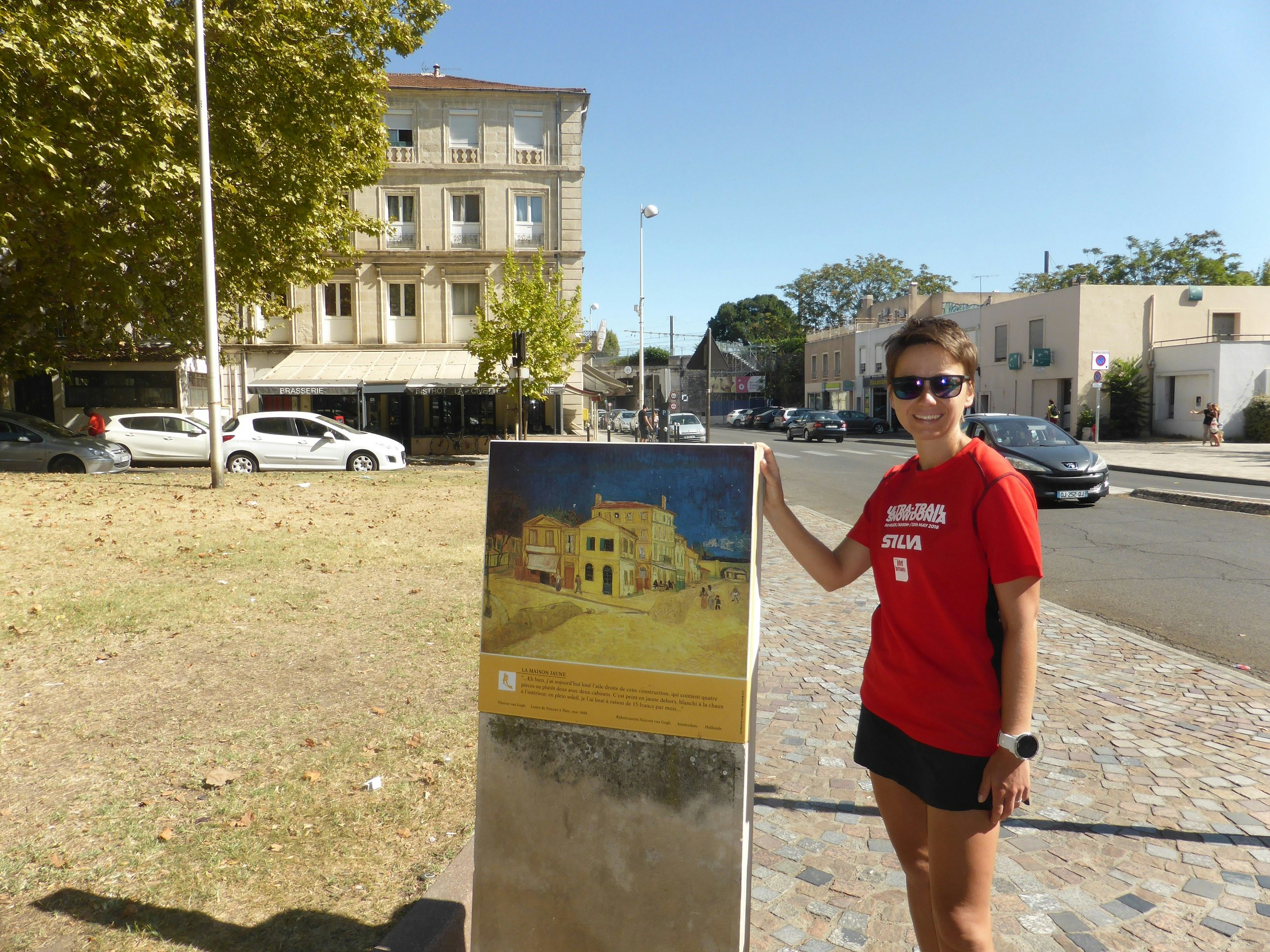 Alecsa standing by a public sign denoting the building featured in Van Gogh's The Yellow House; in the background is the same house.