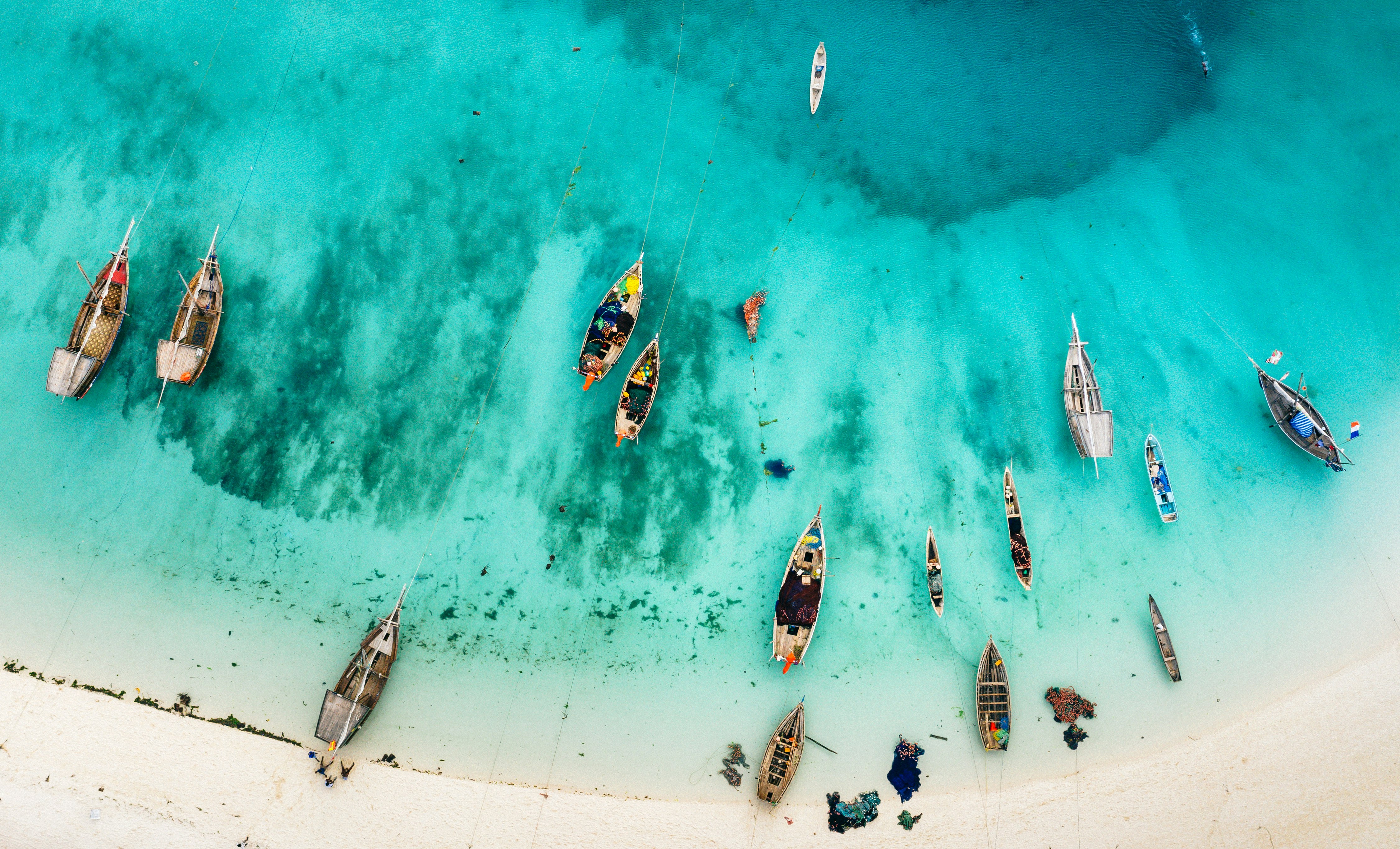 A drone shot shows the crystal blue waters and boats at a beach in Zanzibar. 