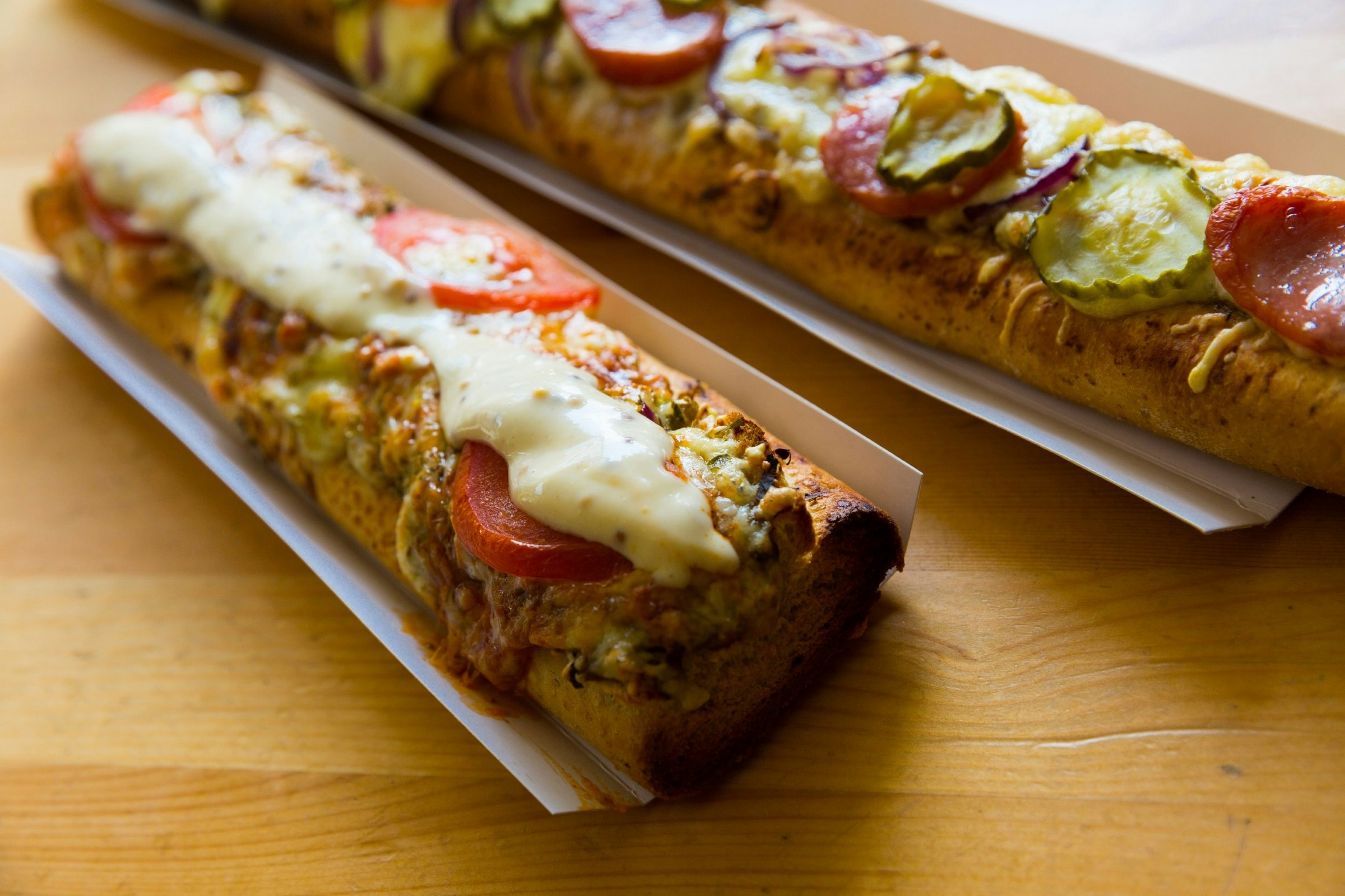 Two half-baguettes filled with sliced vegetables and toasted with melted cheese