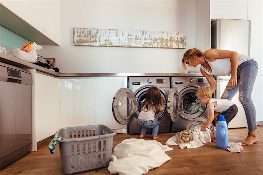 Kids Blog - shutterstock_1083507710 Two toddlers help a woman put laundry in the washing machine