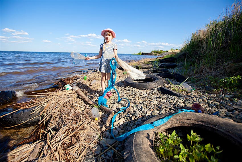 Kids Blog - shutterstock_141493540 A girl in a sun hat picks up litter on a pebbly coastline