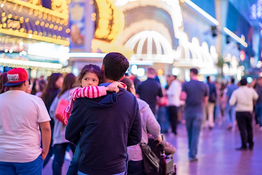 Kids Blog - shutterstock_767621836 An adult carries a child on the brightly-lit streets of Las Vegas