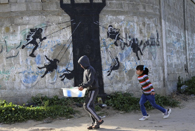 Palestinian children walk next to a mural of children using an Israeli army watch tower as a carnival ride painted by British street graffiti artist Banksy, on the main road in Beit Lahiya, in the northern Gaza Strip.