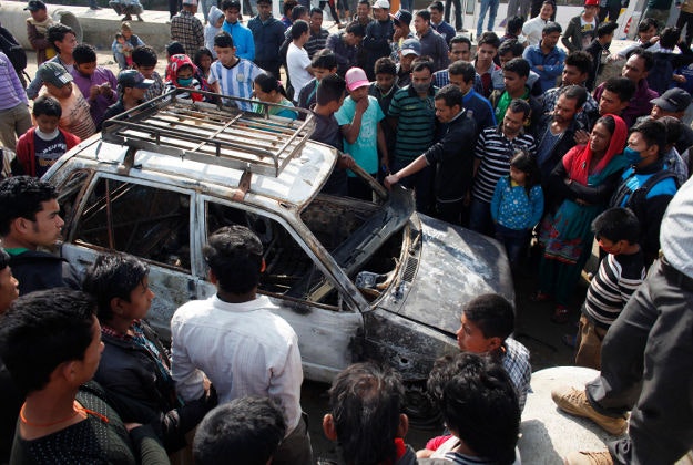 Nepalese people gather around the wreckage of a car burned by demonstrators during a general strike called by the alliance of 30 opposition parties, demanding the Himalayan nation's new constitution draft be passed by a national consensus, in Kathmandu, Nepal, Tuesday, April 7, 2015. Image by AP Photo/Niranjan Shresta.