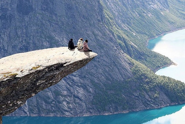 Three people sit atop Trolltunga, Norway.