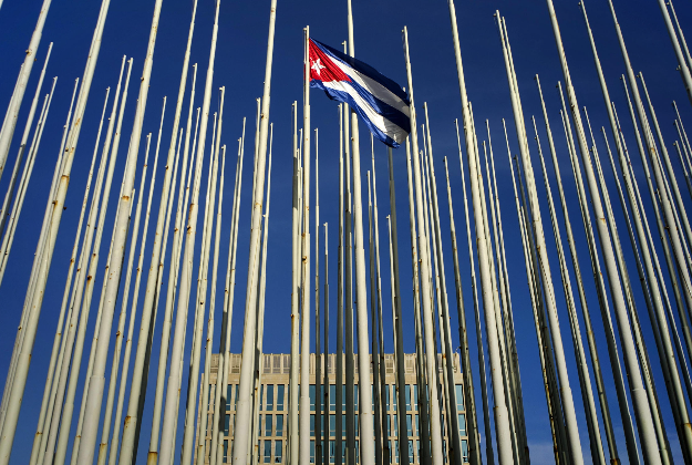 A Cuban flag flies among empty flag polls near the U.S. Interests Section building, behind, in Havana, Sunday, July 19, 2015.