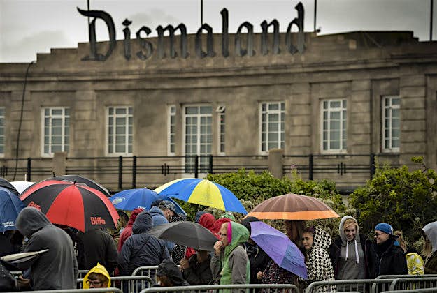 Travel News - dismaland 2 People queue in the rain to buy tickets for Banksy's exhibition theme park 'Dismaland' at Weston-super-Mare, Somerset.