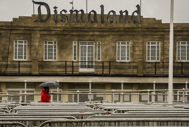 A man holding a umbrella walks past Banksy's exhibition theme park 'Dismaland' at Weston-super-Mare, Somerset, where rain continues to fall on a grey and wet day.