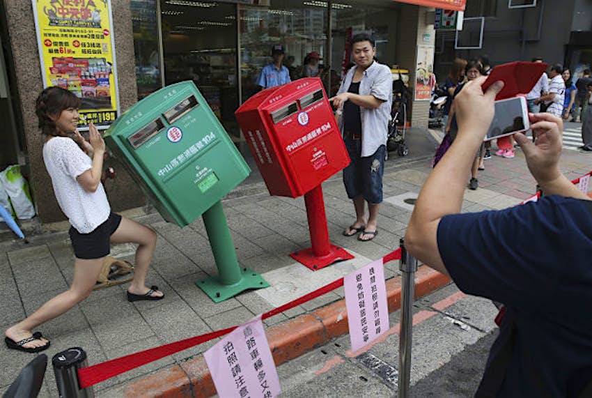 Travel News - taiwan typhoon postboxes 1 A couple poses for photographs next to a pair of roadside mailboxes that were uniformly bent by a falling signboard during a typhoon earlier this month in Taipei, Taiwan.