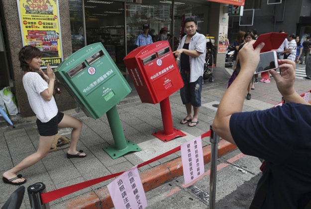 A couple poses for photographs next to a pair of roadside mailboxes that were uniformly bent by a falling signboard during a typhoon earlier this month in Taipei, Taiwan.