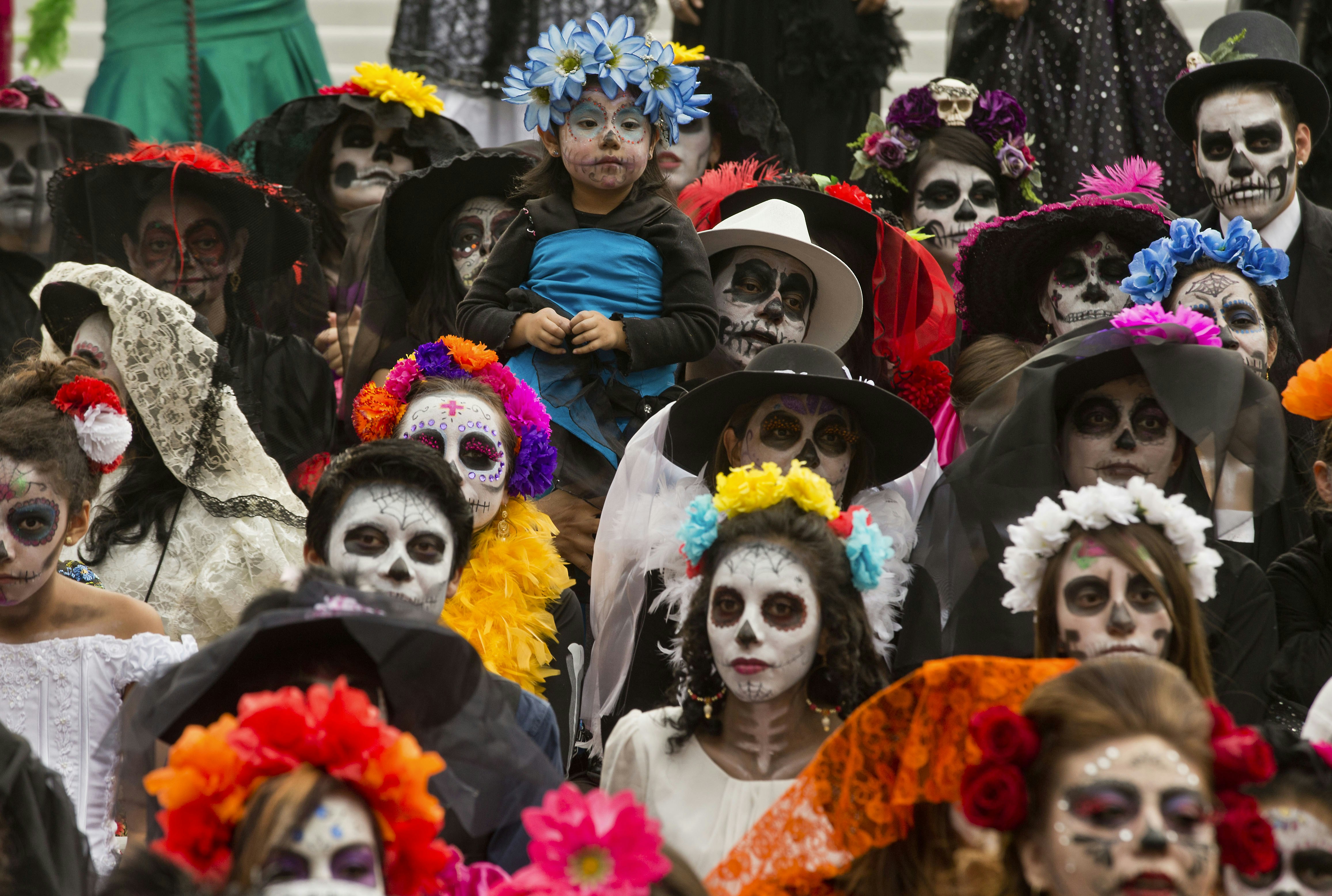 A girl in costume is held up during a Catrina Fest to commemorate Day of the Dead, a holiday that honors the deceased, in Mexico City, Sunday, Nov. 1, 2015.