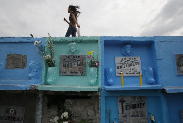 A Filipino girl holding a flower walks on top of tombs that are placed on top of each other inside Manila's North cemetery, Philippines on Sunday Nov. 1, 2015. Filipinos flocked to cemeteries and memorial parks to remember their dead as they observe All Saints Day in this predominantly Roman Catholic country.