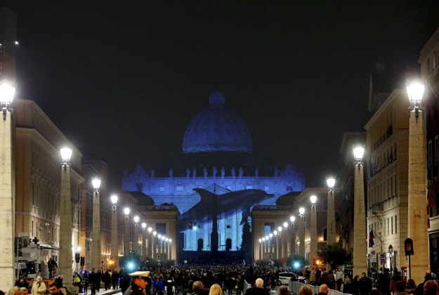People gather to watch images projected on the facade of St. Peter's Basilica, at the Vatican, Tuesday, Dec. 8, 2015. The Vatican is lending itself to environmentalism with a special public art installation timed to coincide with the final stretch of climate negotiations in Paris. On Tuesday night, the facade of St. Peter's Basilica has been turned into a massive backdrop for a photo light show about nature organized by several humanitarian organizations. Organizers offered the installation as a gift to Francis to mark his Holy Year of Mercy, which began Tuesday. 
