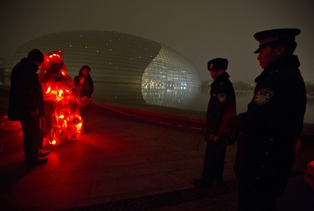 Chinese police officer questions performance artist Kong Ning as she wears a gown with glowing red light and stop signs to raise awareness of the smog enveloping Beijing, China, Wednesday, Dec. 9, 2015. Beijing residents stayed indoors, schools were closed and limits on cars, factories and construction sites kept pollution from spiking even higher on Wednesday, the second of three days of restrictions triggered by the city's first red alert for smog. 