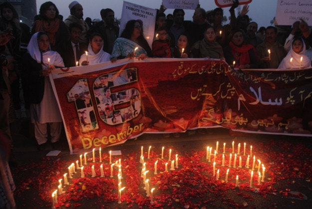 Candles form the initials of the Army Public School as people attend a ceremony in connection with the first anniversary of a school attack in Peshawar, Wednesday, Dec. 16, 2015 in Lahore, Pakistan. Pakistan has closed schools across the country for a day on the anniversary of last year's Taliban attack that killed over 150 people, 144 of them schoolchildren. Banner reads "we pay tribute to victims." 