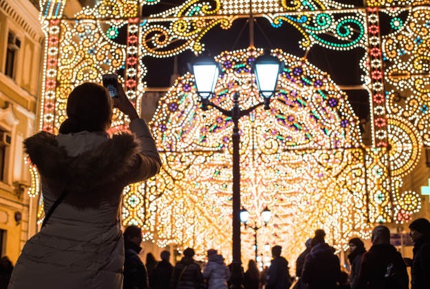 A tourist takes a photo as people walk through Nikolskaya street illuminated to celebrate the upcoming Christmas and New Year toward Red Square in Moscow, Russia, Tuesday, Dec. 22, 2015. Russia has been experiencing an unusual warm spell and temperatures climbed as high as 10 degrees Celsius (50 degrees Fahrenheit) in the Russian capital in recent days. 