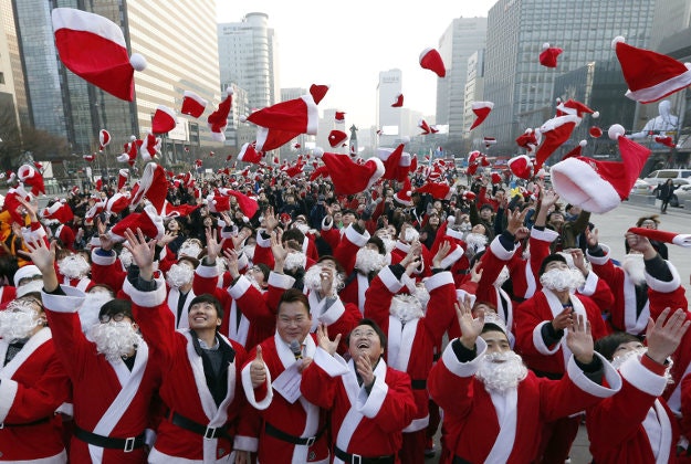 Hundreds of volunteers clad in Santa Claus costumes throw their hats in the air during a Christmas charity event as they gather to deliver gifts for the poor in downtown Seoul, South Korea, Thursday, Dec. 24, 2015. 