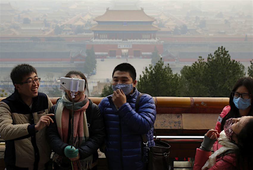 Travel News - beijing smog red alert Visitors, some wearing masks to protect themselves from pollutants, share a light moment as they take a selfie at the Jingshan Park on a polluted day in Beijing.