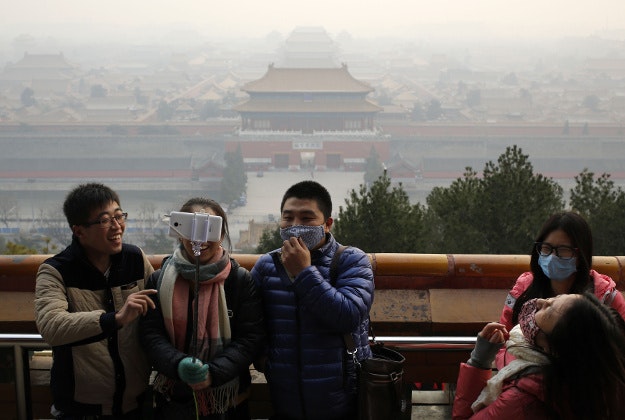 Visitors, some wearing masks to protect themselves from pollutants, share a light moment as they take a selfie at the Jingshan Park on a polluted day in Beijing, Monday, Dec. 7, 2015. Smog shrouded the capital city Monday after authorities in Beijing issued an orange alert on Saturday. 