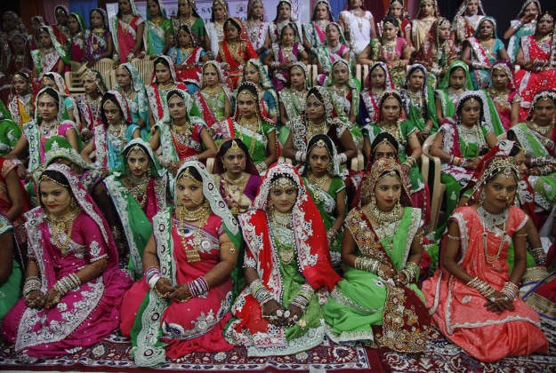 Indian brides sit for a group photo before a mass wedding hosted by a diamond trader in Surat, India, Sunday, Dec. 6, 2015. 151 young couples tied the knot at the mass wedding hosted by Indian diamond trader Mahesh Savani, who has been funding the weddings of fatherless women in the city of Surat for several years. Weddings in India are expensive affairs with the bride's family traditionally expected to pay the groom a large dowry of cash and gifts. Hundreds of people, mostly family members and neighbors of the couple, are hosted at lavish meals over a number of days adding to the costs. 