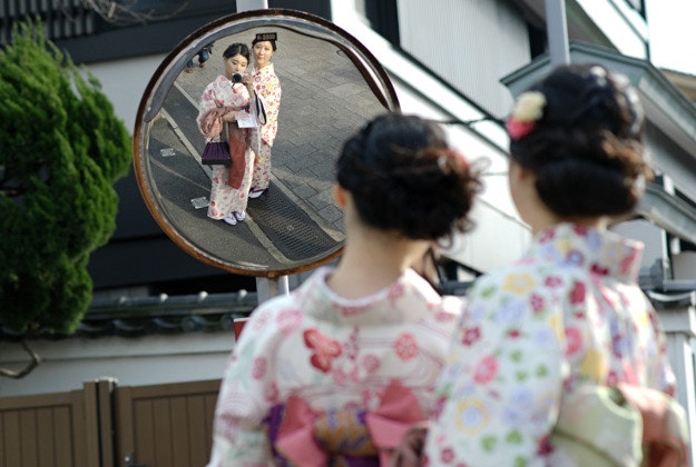 Two Japanese ladies wearing kimonos photograph themselves in a traffic mirror in Kyoto, Japan