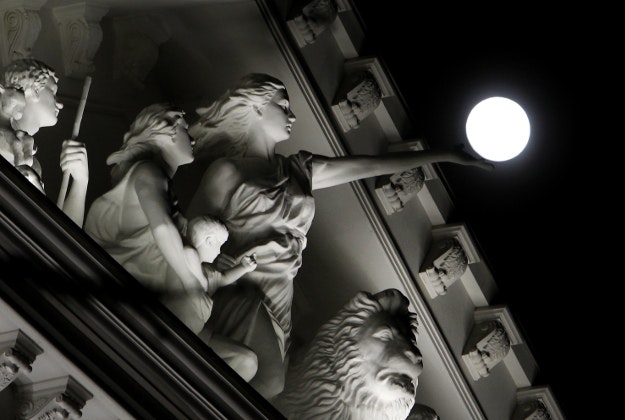 An almost full moon rises over the illuminated sculptures in the tympanum of the Government building in Macedonia's capital Skopje, Sunday, Feb 21, 2016.