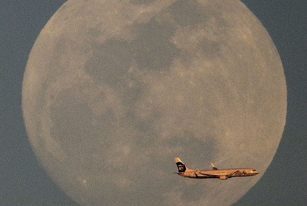An Alaska Airlines jet on approach to Sky Harbor International Airport passes the nearly full moon at it rises in the distance Sunday, Feb. 21, 2016, in Phoenix.