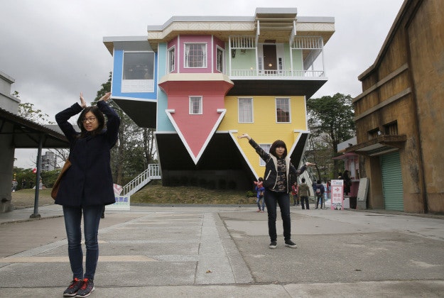 Visitors pose outside of an upside-down house created by a group of Taiwanese architects at the Huashan Creative Park in Taipei, Taiwan, Tuesday, Feb. 23, 2016. With a build price of $600,000 and over 300 square meters (3,230 square feet) of floor space filled with real home furnishings, the upside-down house will continue to be on display to visitors until July 22. 