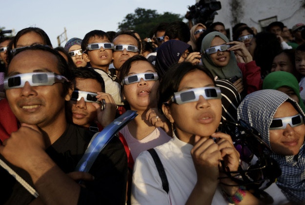 People look up at the sun wearing protective glasses to watch a solar eclipse in Jakarta, Indonesia, Wednesday, March 9, 2016. The rare astronomical event is being witnessed Wednesday along a narrow path that stretches across 12 provinces encompassing three times zones and about 40 million people. 