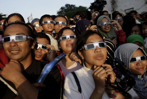 People look up at the sun wearing protective glasses to watch a solar eclipse in Jakarta, Indonesia, Wednesday, March 9, 2016. The rare astronomical event is being witnessed Wednesday along a narrow path that stretches across 12 provinces encompassing three times zones and about 40 million people.