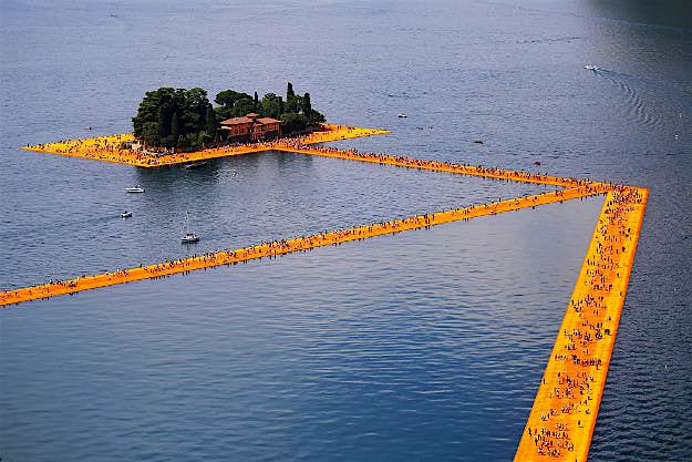 Travel News - GettyImages-541030722 People walk on the monumental installation entitled 'The Floating Piers' created by artist Christo Vladimirov Javacheff on Iseo Lake, in northern Italy, on June 18, 2016. Some 200,000 floating cubes create a 3-kilometers runway connecting the village of Sulzano to the small island of Monte Isola on the Iseo Lake for a 16-day outdoor installation.