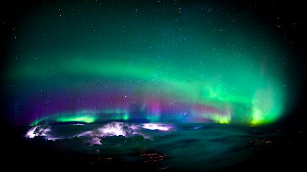 Travel News - HEAVENLY WEATHER FROM A PLANE Lightning lights up inside some clouds as the Northern Lights cover the sky above it.