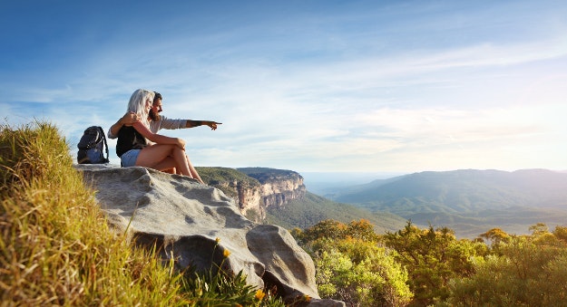 Young traveling couple having rest on the rock and enjoying view in Blue Mountains in Australia. 