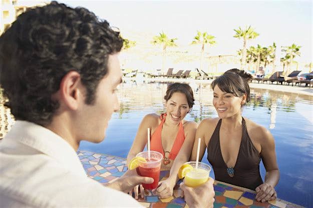 Travel News - Two Hispanic women getting drinks at a hotel pool bar Be careful when charging poolside drinks and snacks to your room. Image: Plush Studios/Bill Reitzel