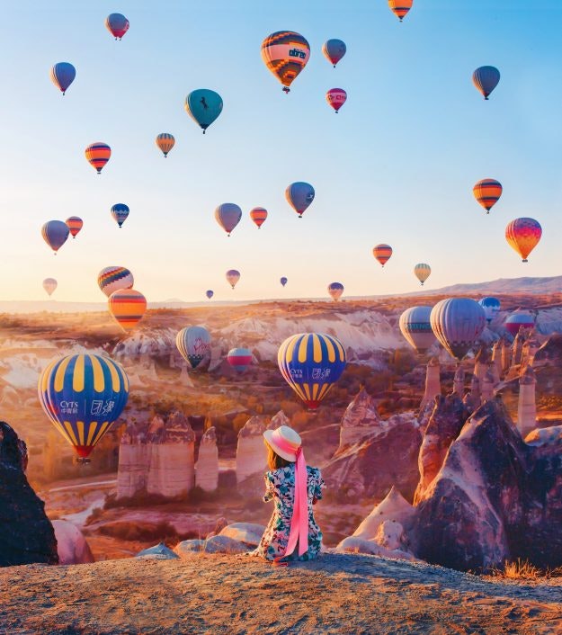 A model in a colourful dress and hat watches the balloons.