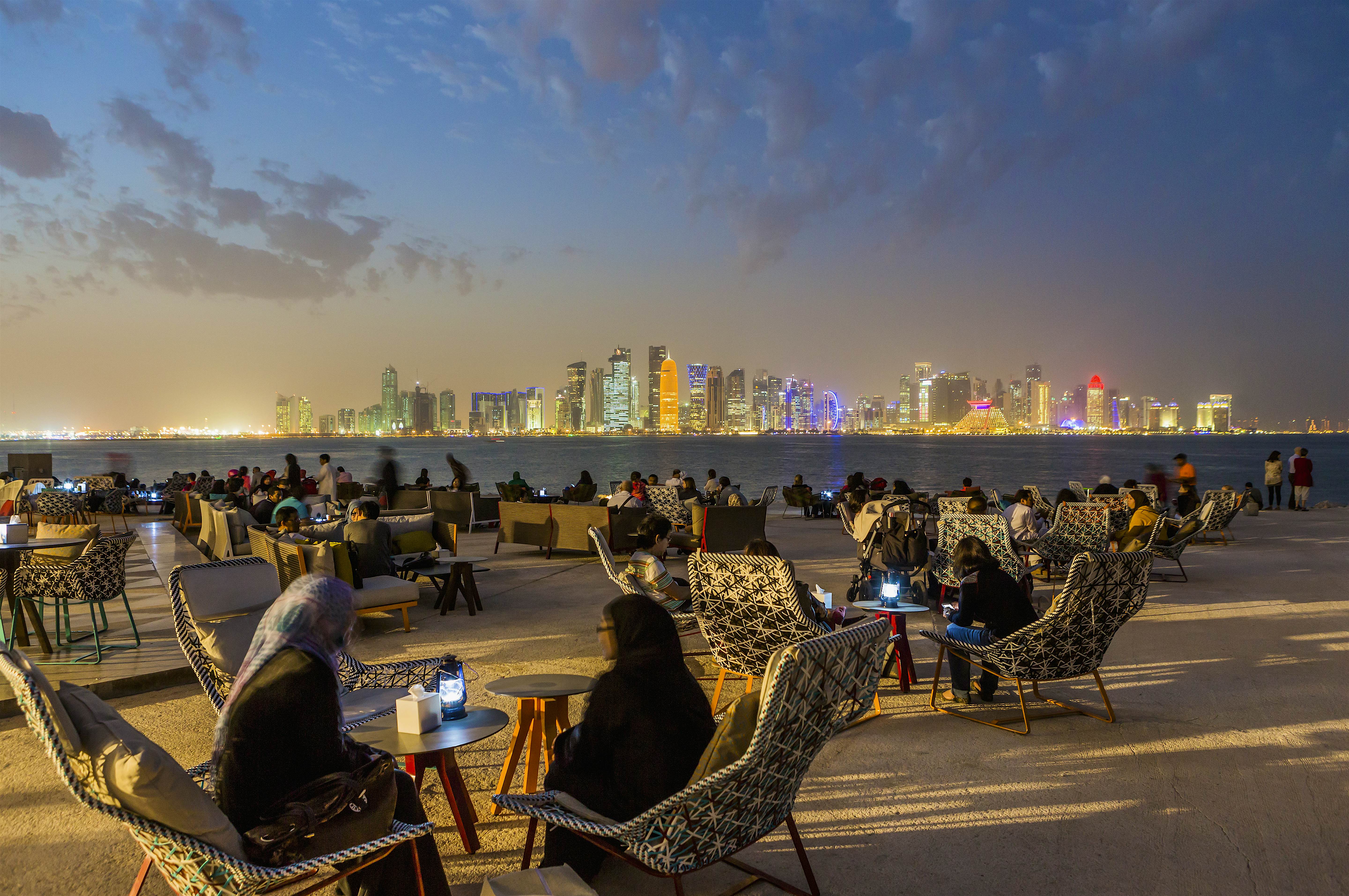 Travel News - Doha Corniche, Museum of Islamic Art (MIA) Park Doha Corniche, Museum of Islamic Art (MIA) Park, people at MIA Park Café or Kiosk (architect Philippe Starck), on the background Al Dafna district (West Bay Business quarter).