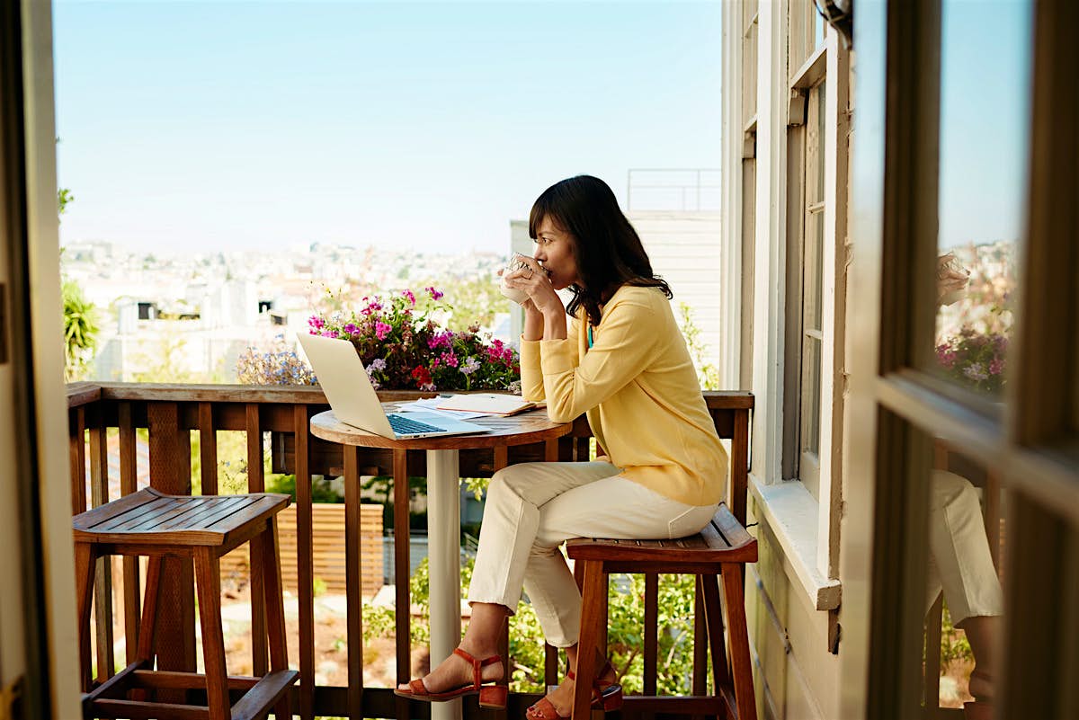 Travel News - secrets of airbnb success A woman sits on the balcony of her Airbnb with laptop