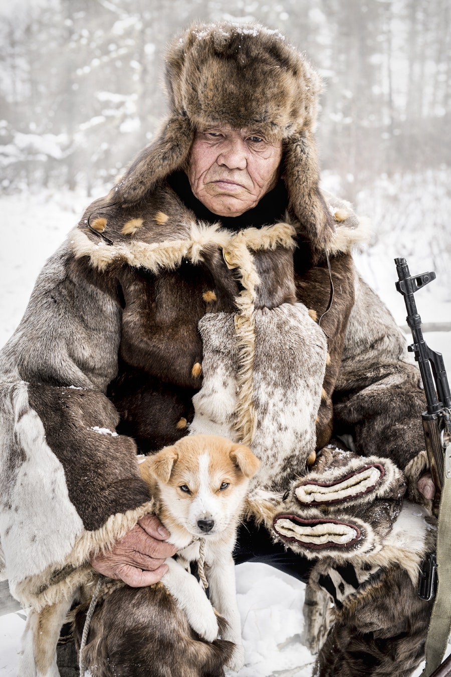 A man poses with a puppy and a rifle. 