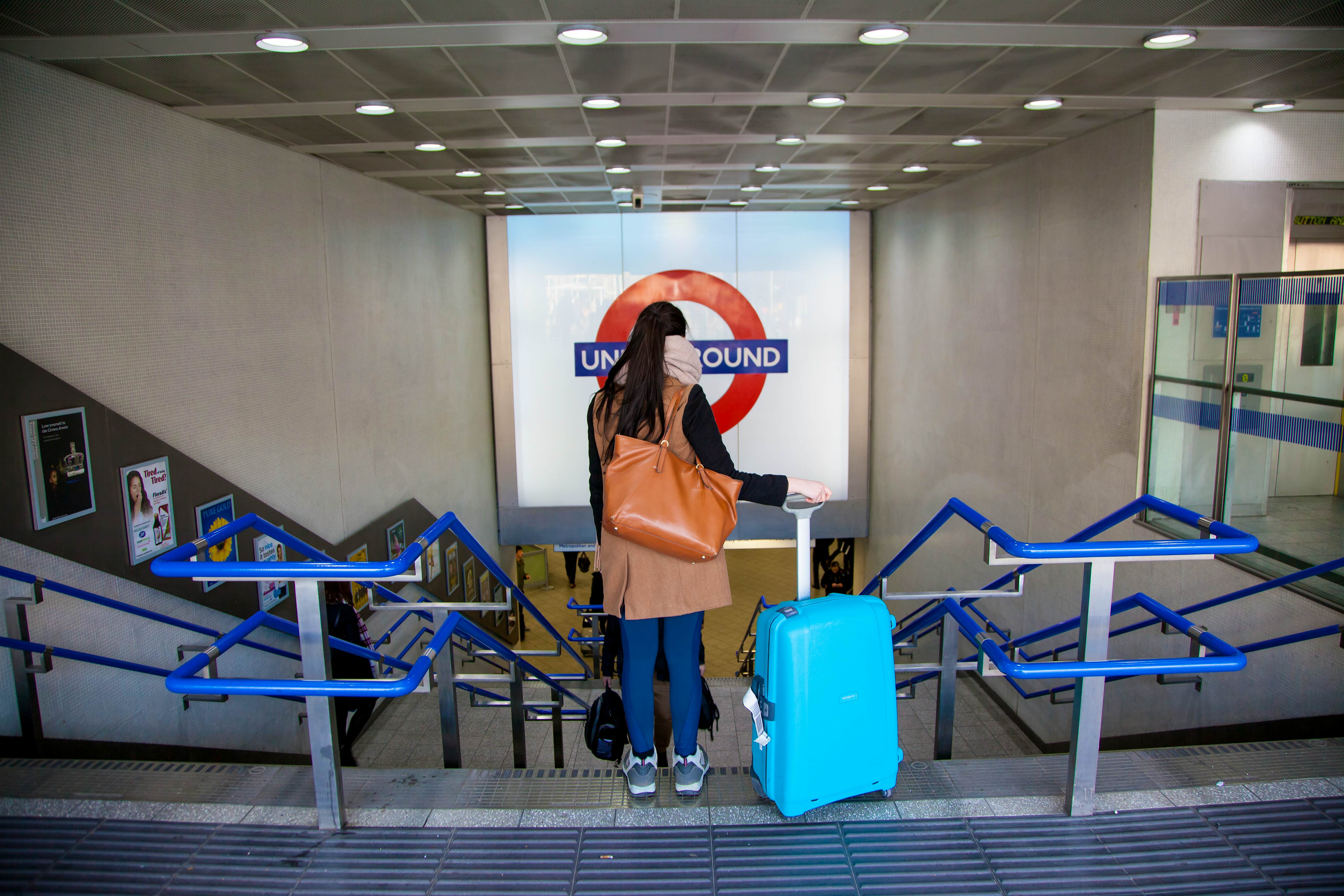 Travel News - Left luggage in London A woman is about to walk down stairs with her suitcase.