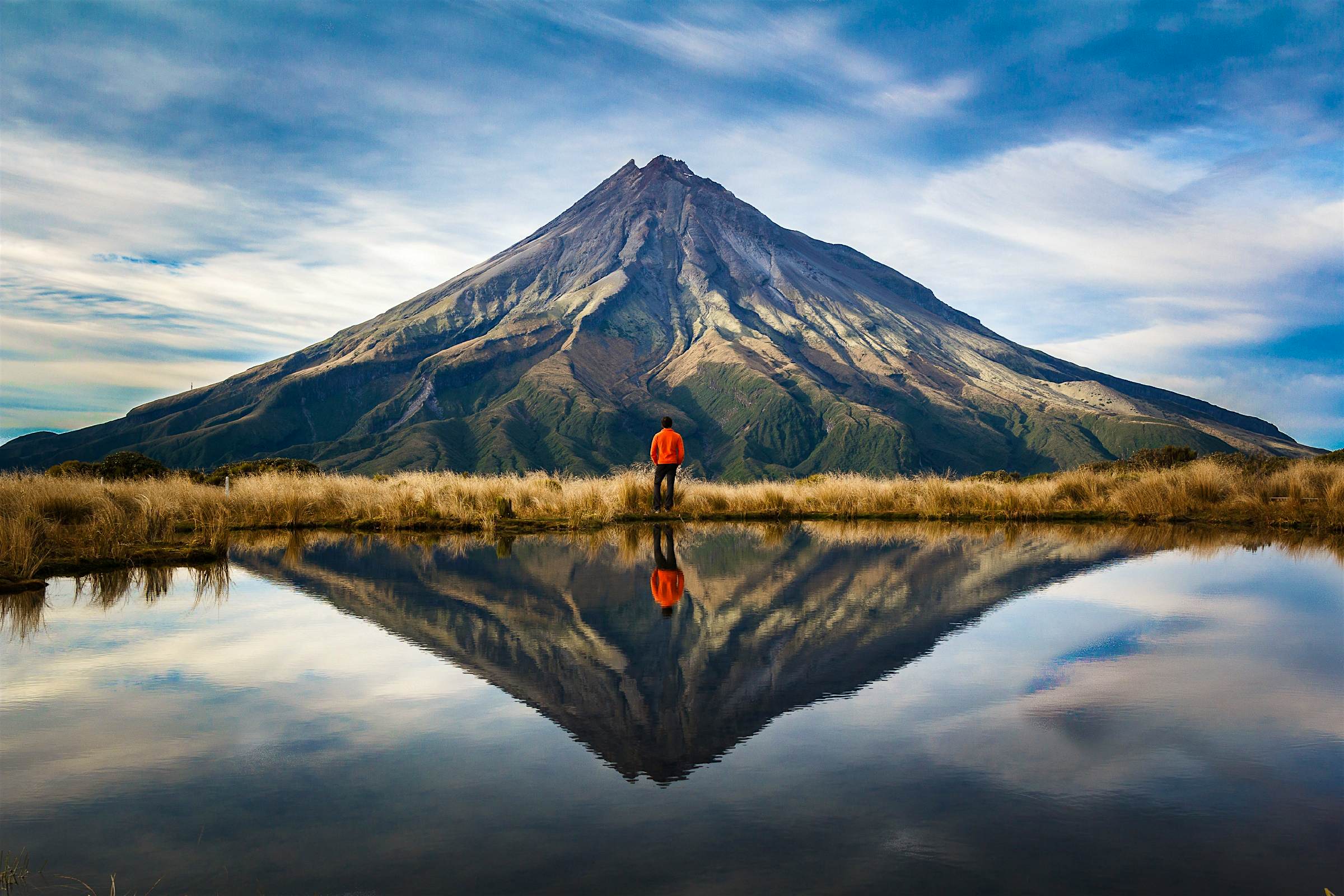 Travel News - new zealand A mountaineer by lake in front of Taranaki volcano. New Zealand.