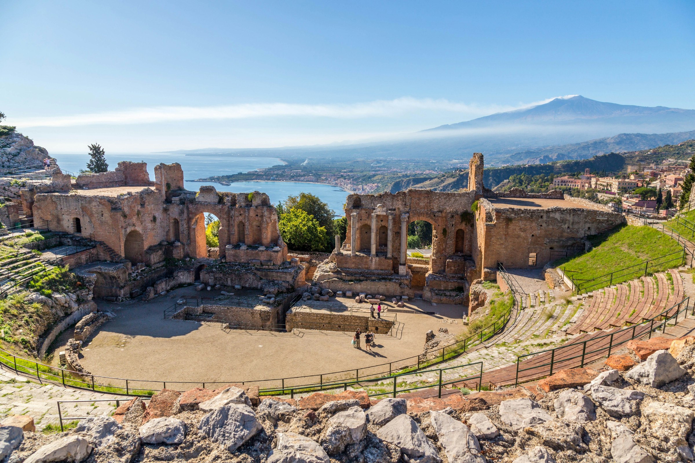 Ruins of the ancient greek theater of Taormina, Sicily the Etna with its double snook tail in the background above the morning sun lit Giardini-Naxos bay of the Ionian see.