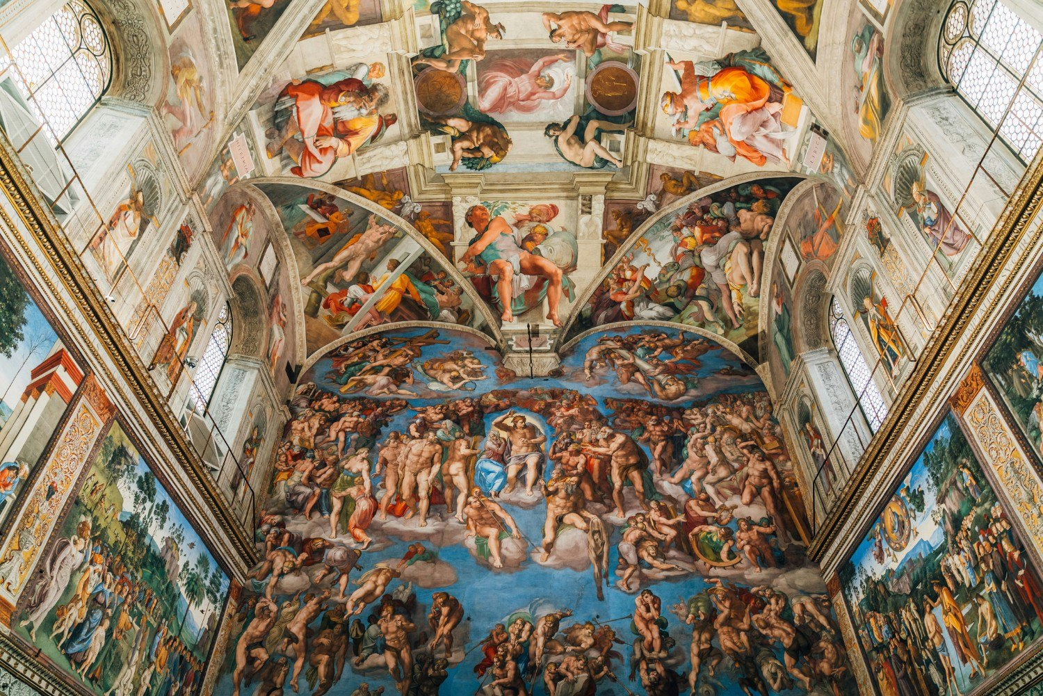 A low angle view of a mural in the Sistine Chapel with people looking at it