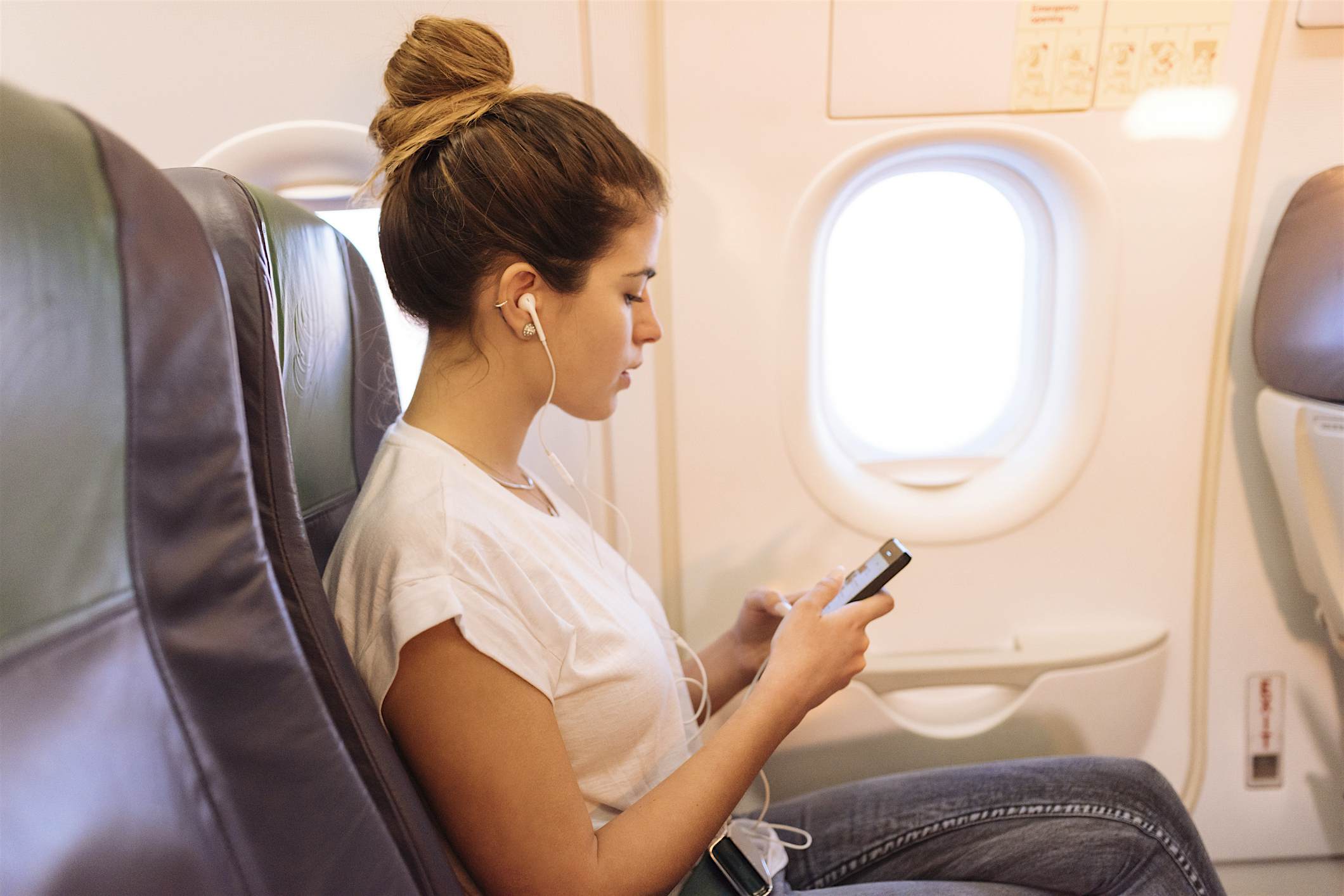 Travel News - netflix oung woman on airplane choosing music on smartphone.
